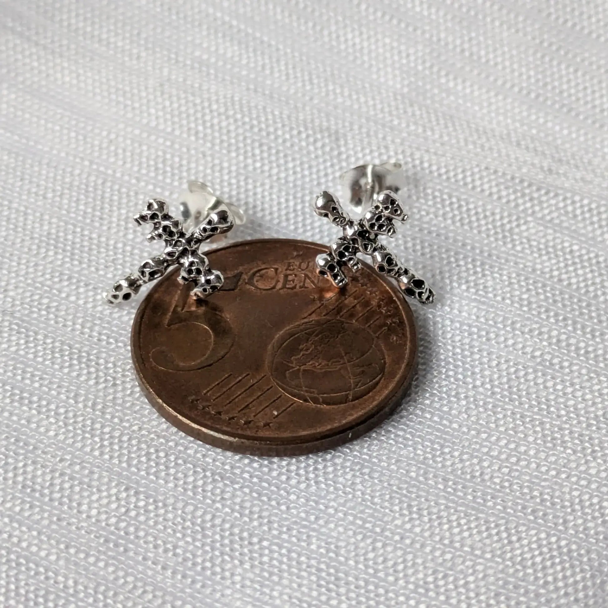 Größenvergleich der silbernen Skull-Ohrstecker auf einer 5-Cent-Münze.