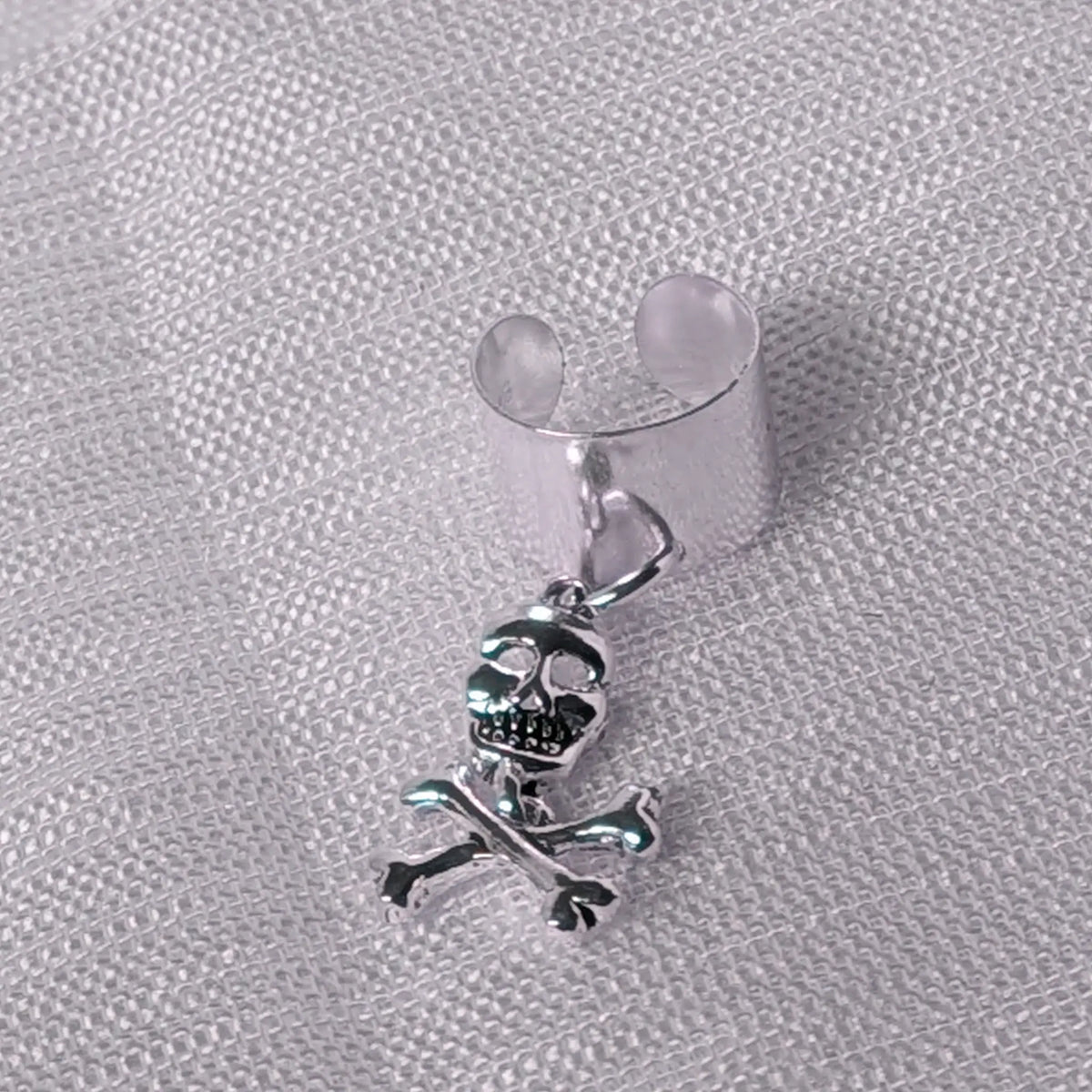 Detaillierte Nahaufnahme einer breiten 925 Silber Ohrklemme mit frei schwingendem Totenkopf-Anhänger und gekreuzten Knochen.