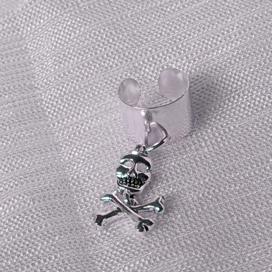Detaillierte Nahaufnahme einer breiten 925 Silber Ohrklemme mit frei schwingendem Totenkopf-Anhänger und gekreuzten Knochen.