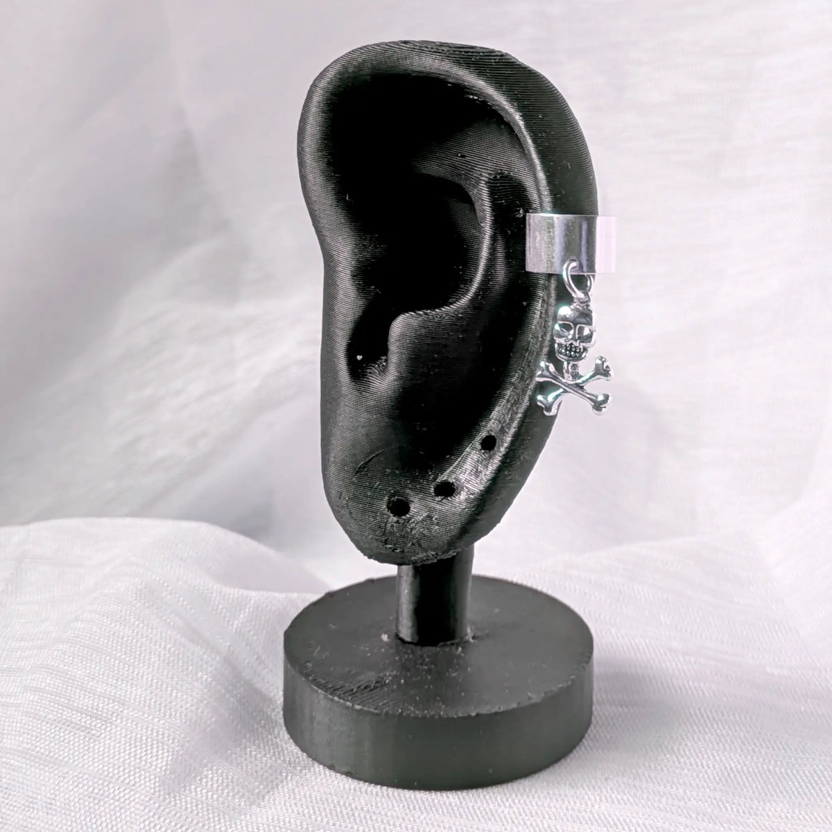 Rockiger Silber-Earcuff mit Totenkopf, sicher getragen am seitlichen Knorpel eines schwarzen Ohr-Displays.