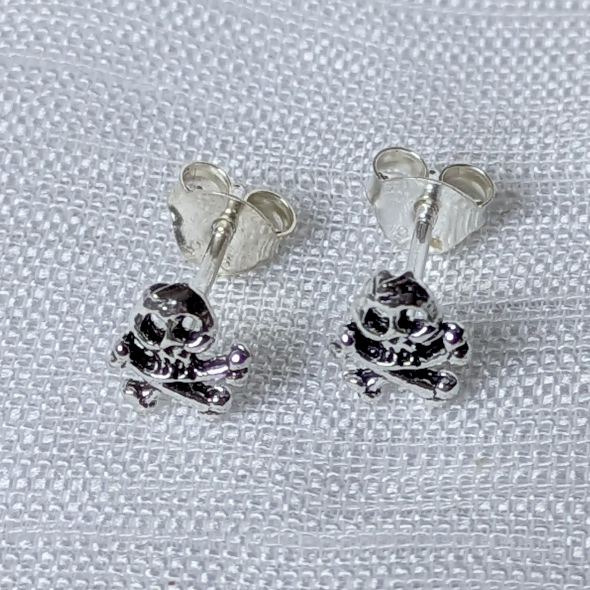 Frontalansicht der silbernen Skull Ohrstecker mit gekreuzten Knochen.`