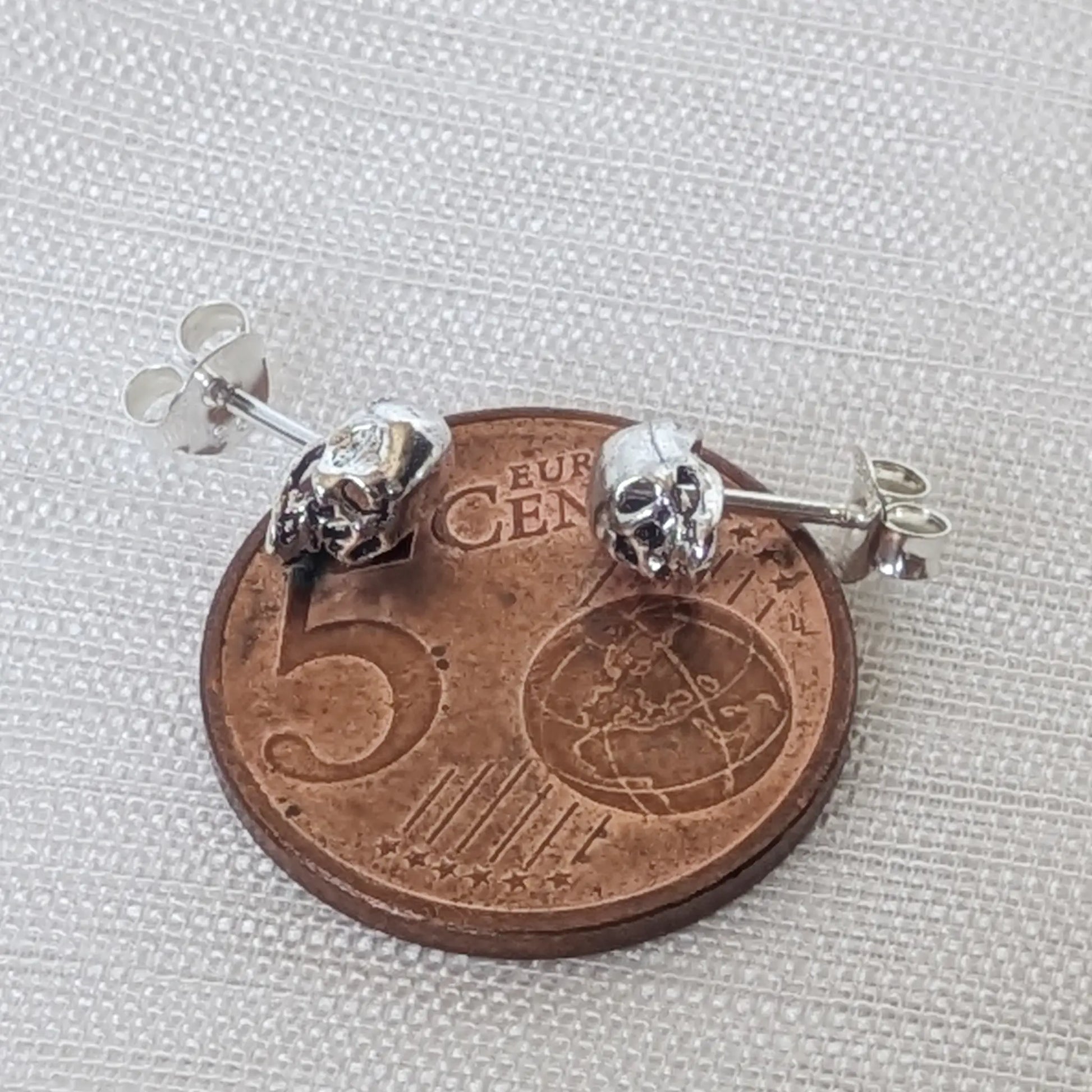 Größenvergleich: Der filigrane silberne Totenkopf Ohrring liegt auf einer 5-Cent-Münze.