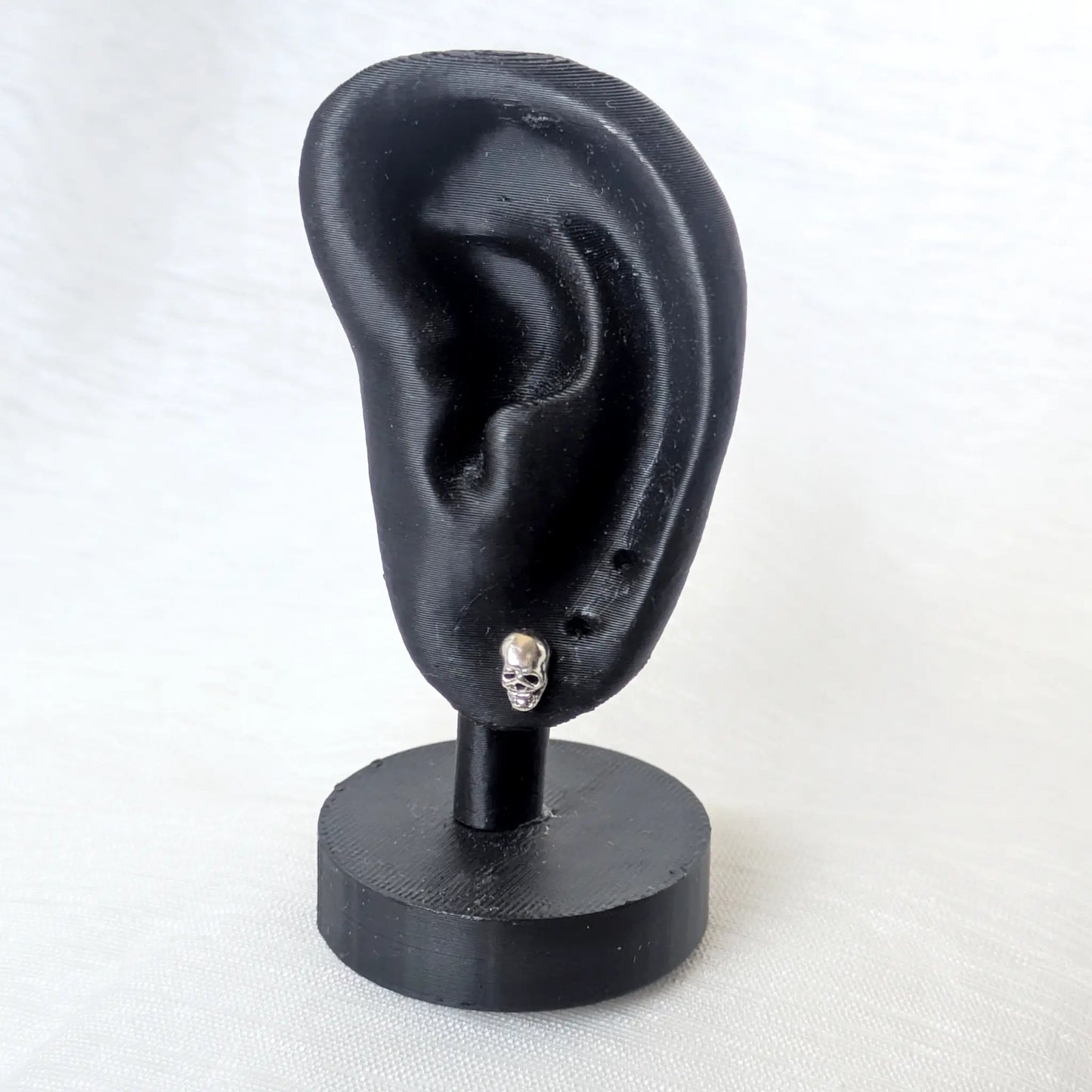 Kompakter Totenkopf Ohrstecker aus 925 Silber getragen an einem schwarzen Ohr-Display zur Veranschaulichung der Größe.