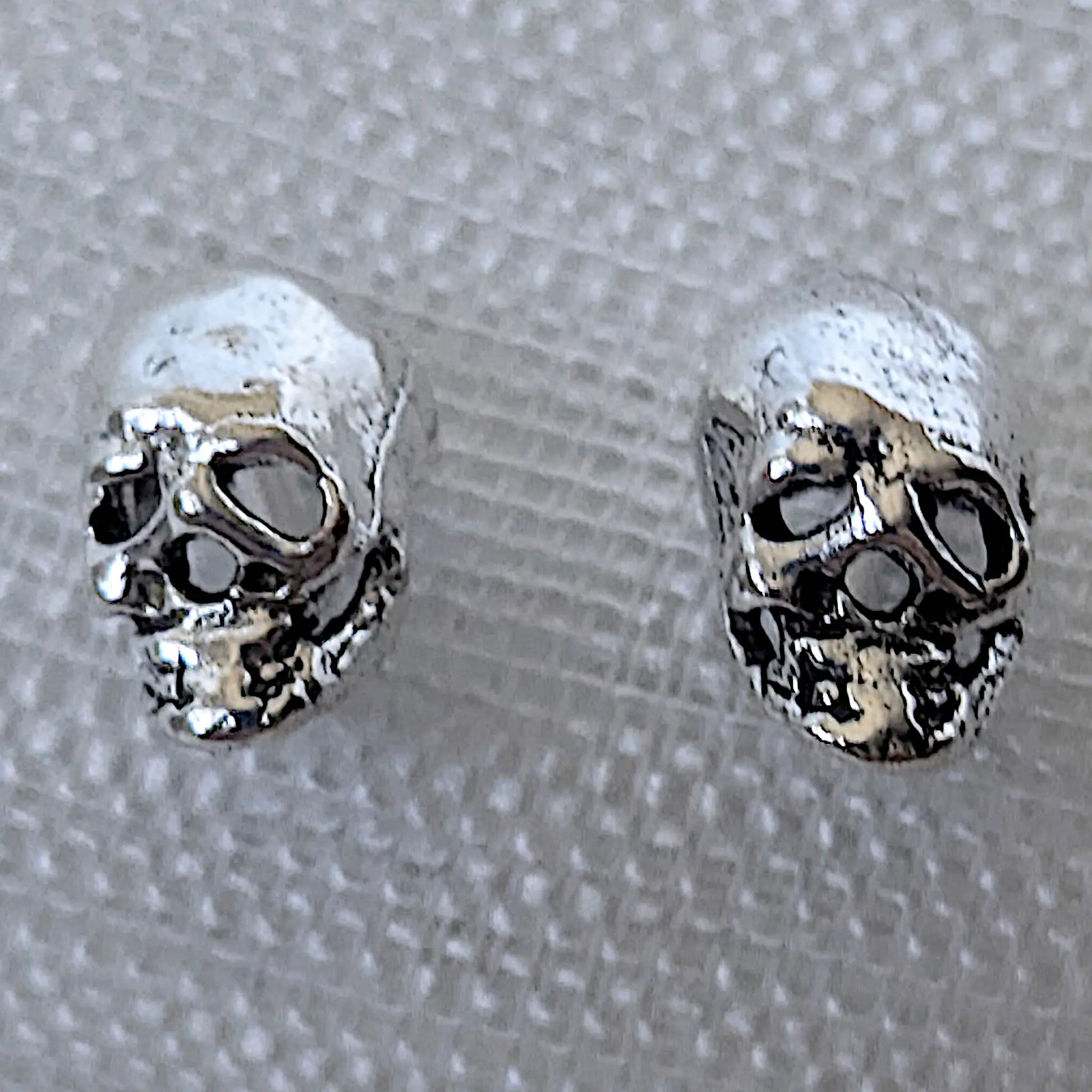 Nahaufnahme von zwei detailreichen Totenkopf Ohrsteckern aus glänzendem 925 Sterling Silber mit feinen Konturen.