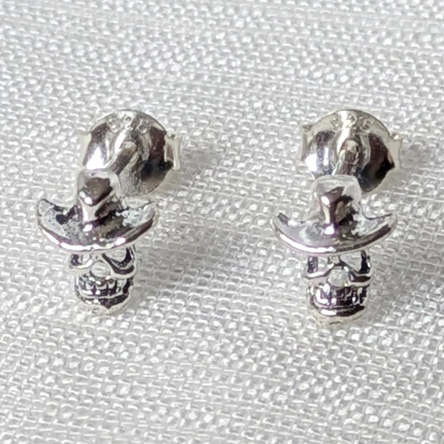 Frontalansicht der silbernen Skull Ohrringe mit Cowboyhut aus echtem Silber auf strukturiertem Hintergrund.
