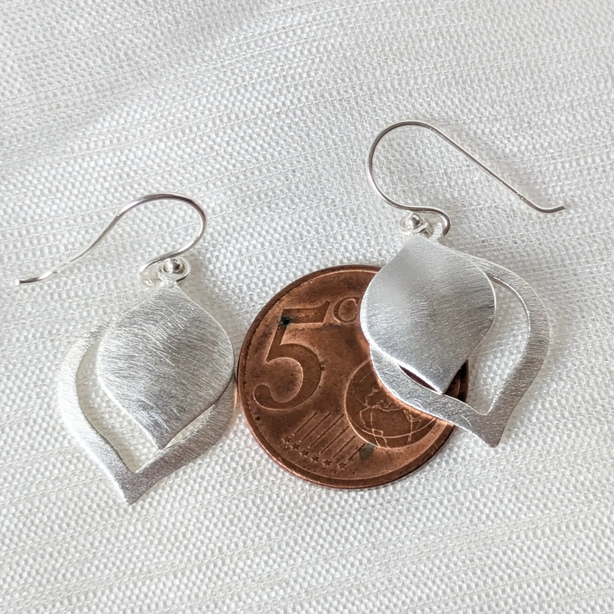 Ein mattierter 925 Silber Ohrhänger in Tropfenform liegt direkt auf einer 5-Cent-Münze.