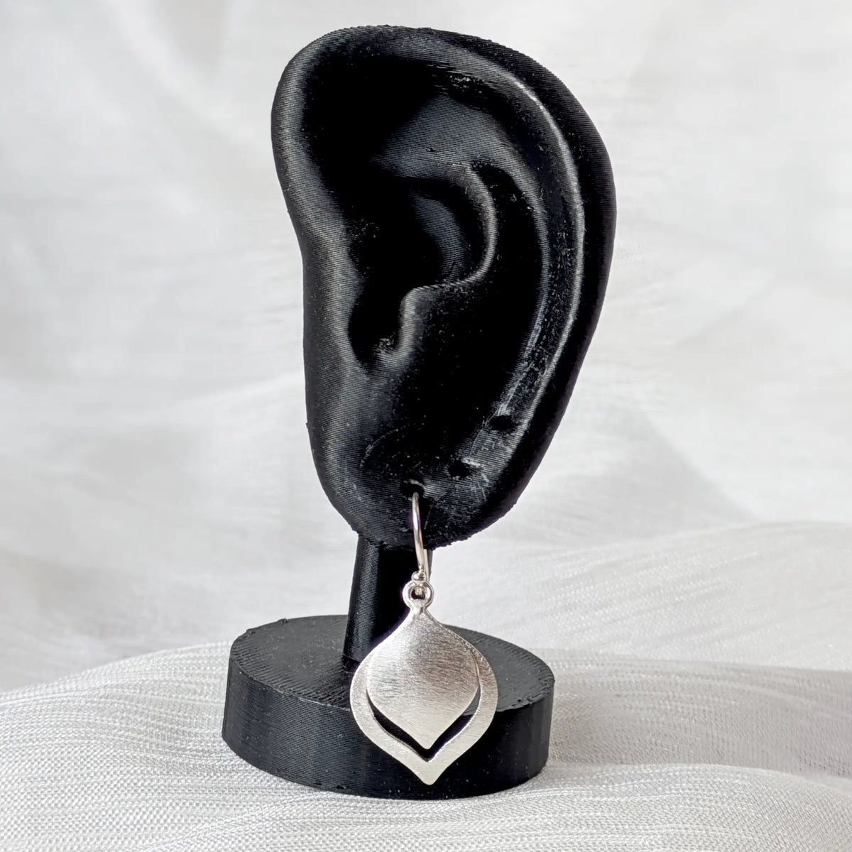 Ein mattierter Silber-Ohrhänger präsentiert an einem schwarzen 3D-Ohr-Display zur Veranschaulichung der Tragegröße.