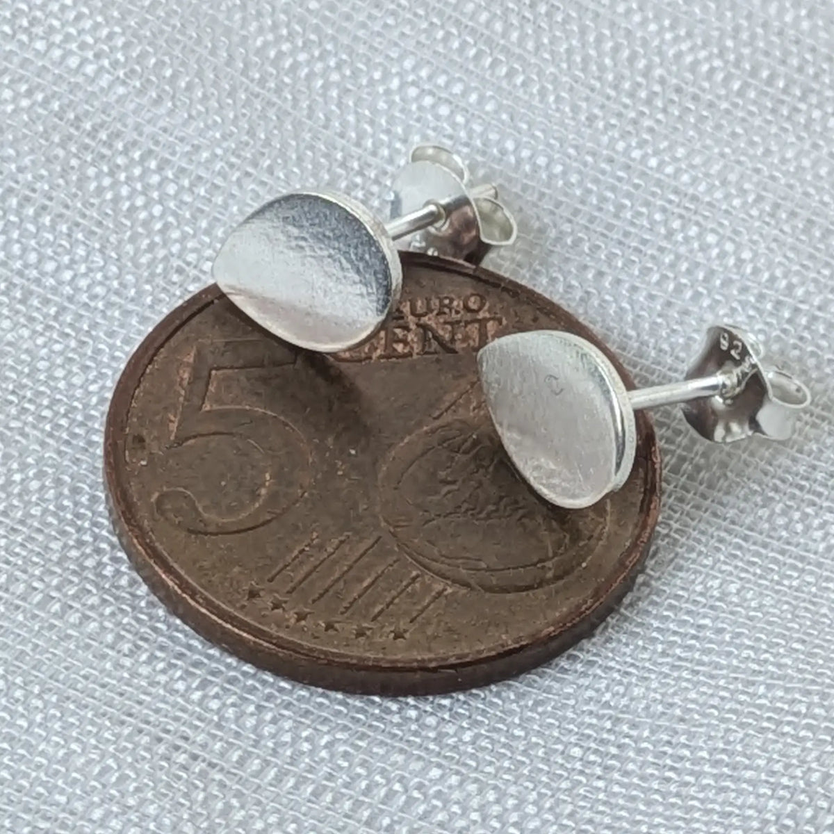 Tropfenförmige Silber-Ohrstecker liegend auf einer 5-Cent-Münze zum Größenvergleich.