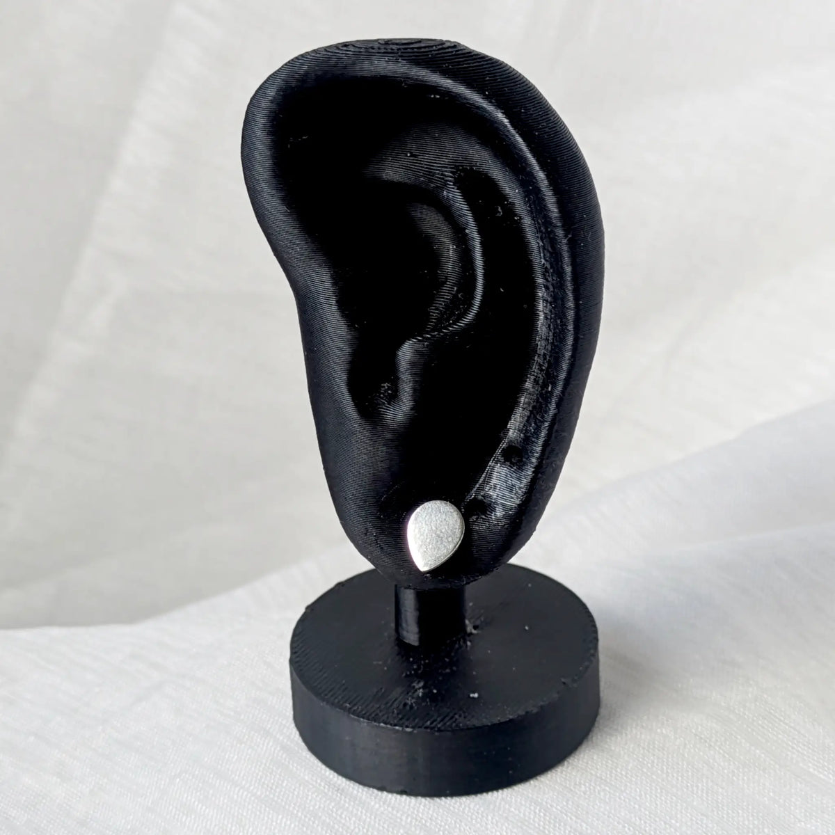 Silberner Tropfen-Ohrstecker elegant präsentiert an einem schwarzen Ohr-Display.