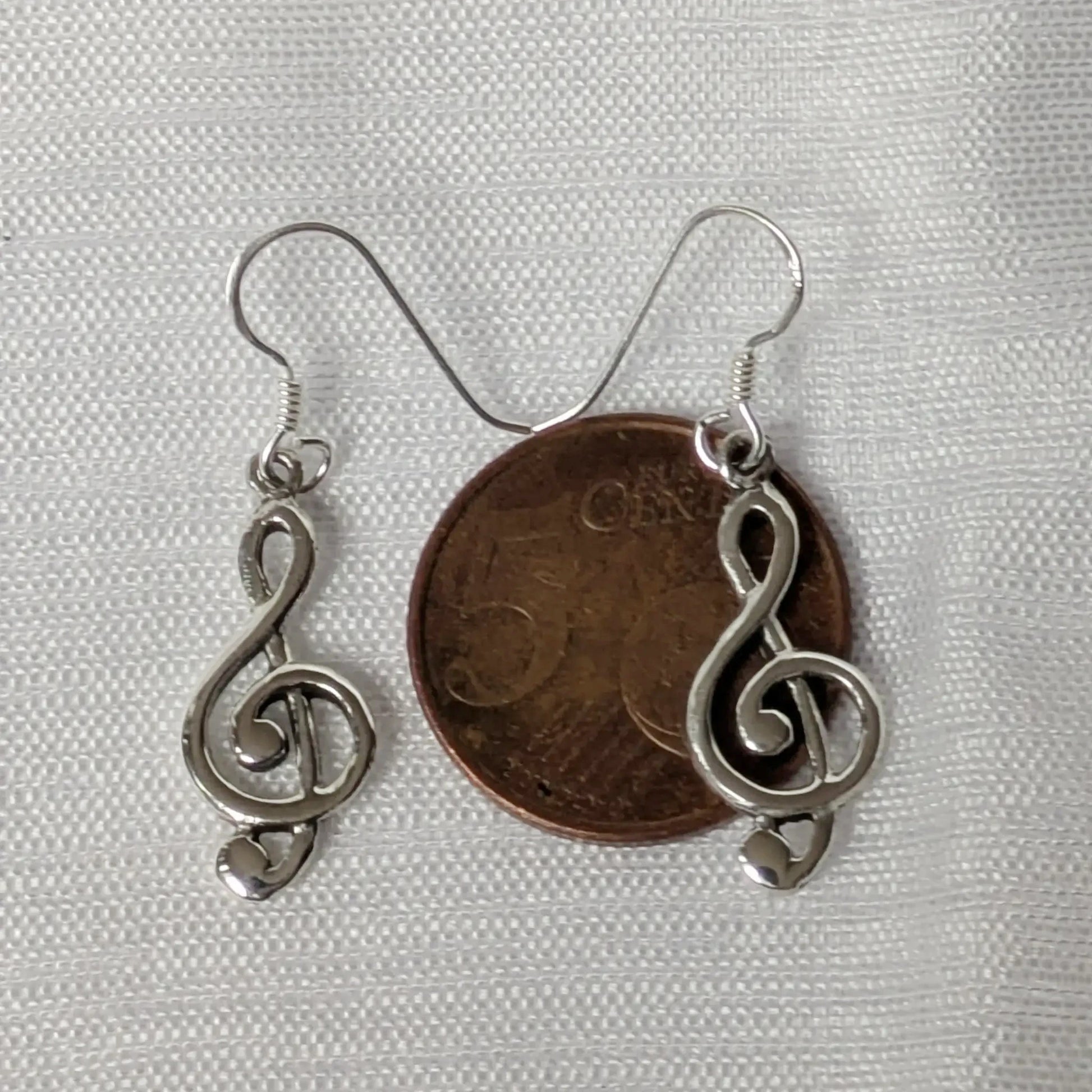 Größenvergleich der silbernen Notenschlüssel Ohrringe neben einer 5-Cent-Münze.