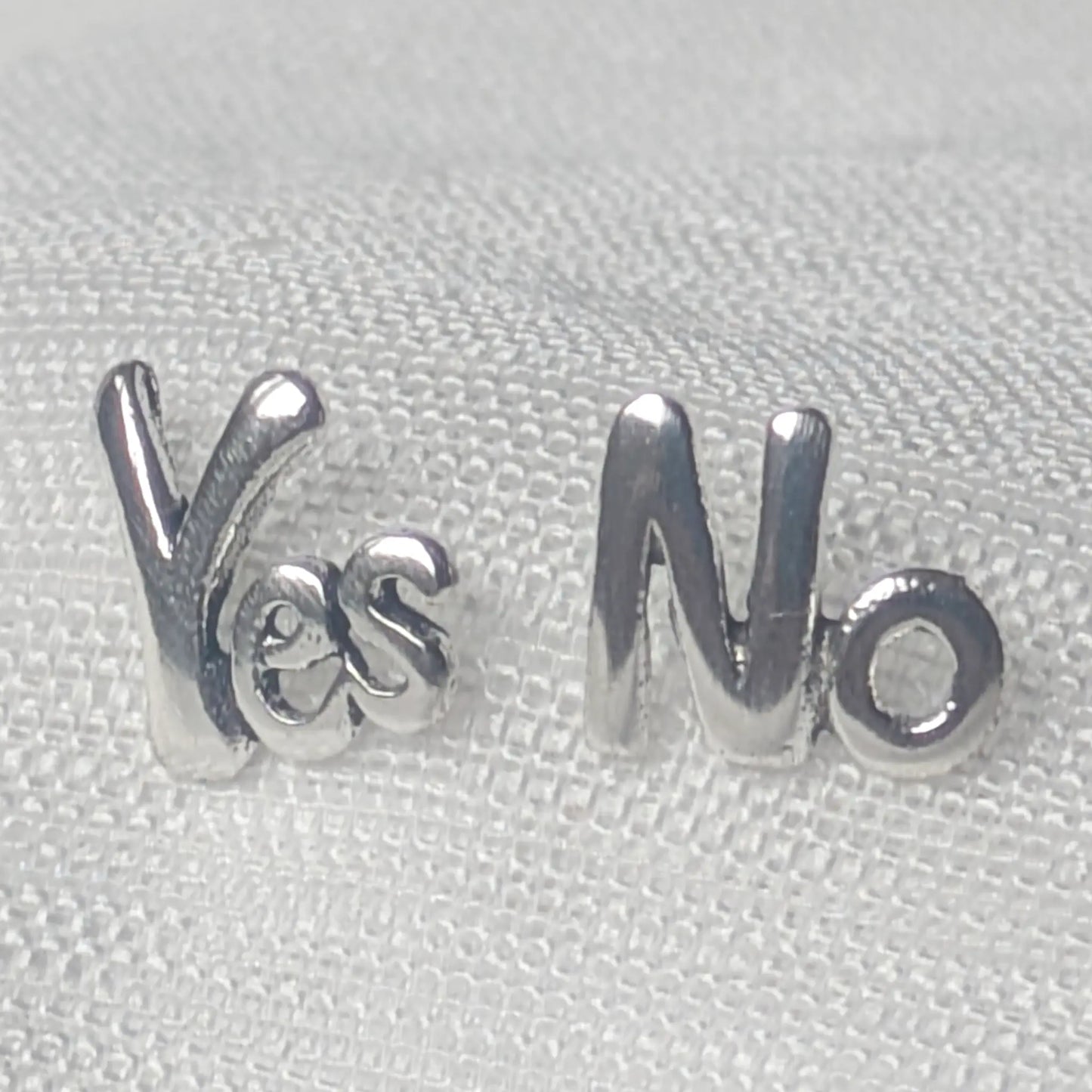 Nahaufnahme der asymmetrischen Yes No Ohrstecker aus glänzendem 925 Sterling Silber auf hellem Stoff.