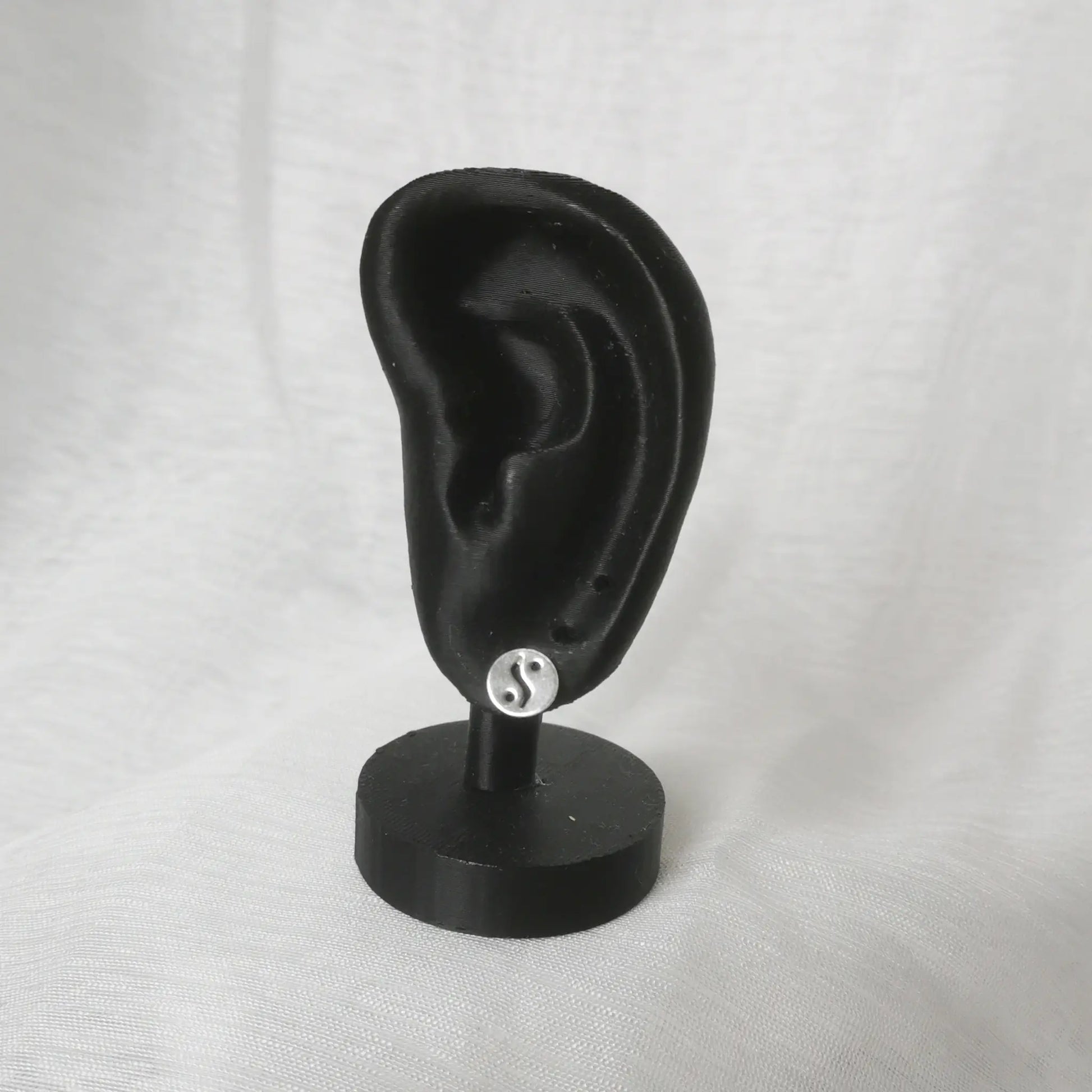 Proportionale Darstellung der Yin Yang Ohrstecker an einem schwarzen Modell-Ohr.