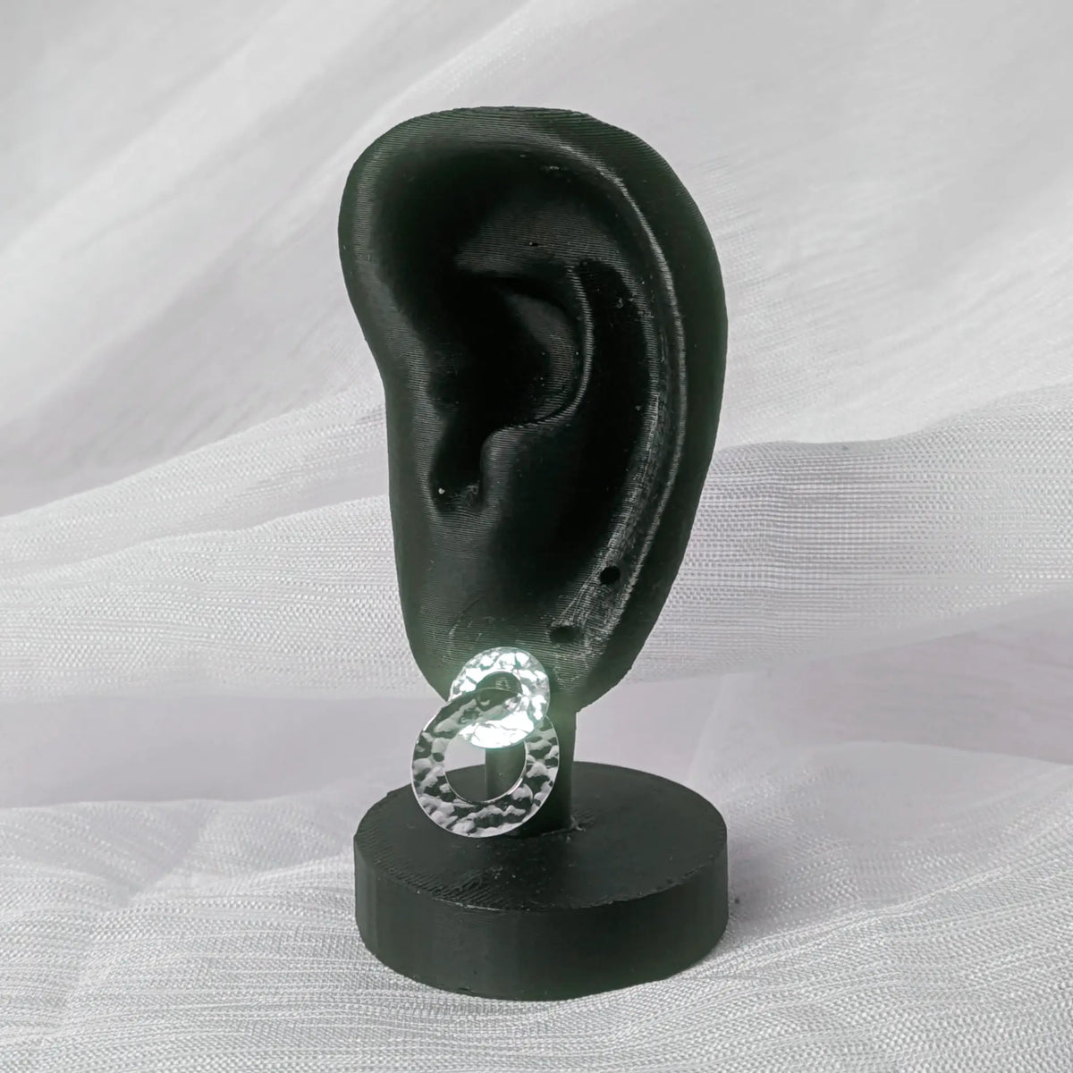 Gehämmerter Silber-Ohrstecker hängend an einem schwarzen 3D-Ohr-Display zur Größendarstellung.